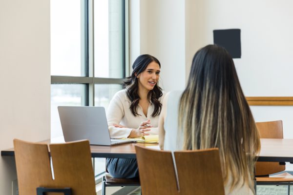 The young adult  business owner gestures as she asks the unrecognizable female job applicant questions during the interview.