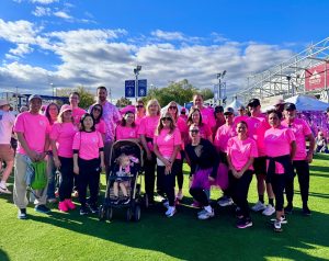 Group of people in pink shirts participating in an outdoor charity event under a blue sky.