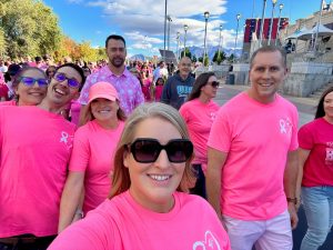 Group of people in pink shirts participating in a charity walk outdoors on a sunny day.