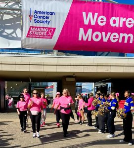 People in pink shirts at American Cancer Society charity event with cheerleaders nearby.