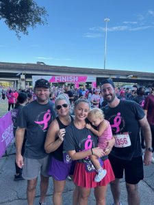 Group of people at a breast cancer awareness event finish line, wearing pink ribbon shirts.