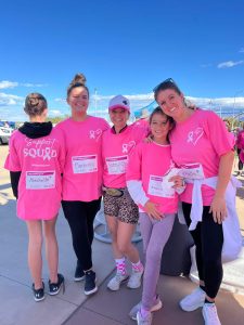 A group of women wearing pink Support Squad t-shirts stand together under a clear blue sky.