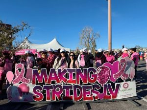 People gathered at a Making Strides LV breast cancer awareness event with a pink ribbon sign.