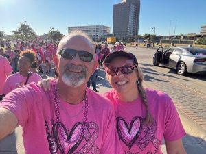 Man and woman in pink shirts at outdoor cancer awareness event with many participants in background.
