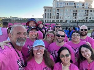 Group of people in pink shirts at outdoor event smiling for a photo with buildings in the background.