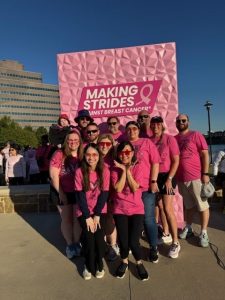 Group in pink shirts at a breast cancer awareness event with Making Strides Against Breast Cancer sign.
