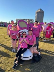 Group in pink shirts posing outdoors with large pink shoe prop.