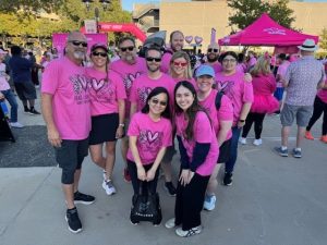 A group of people in pink shirts posing at an outdoor event with pink tents and balloons.