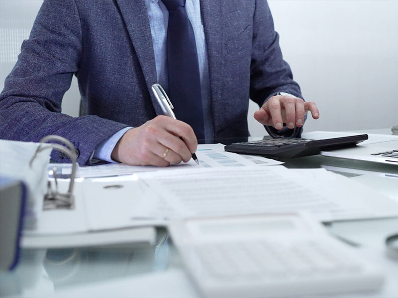 Business person in suit working with calculator and documents at desk.
