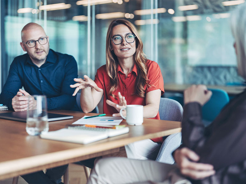 Three people having a business meeting, discussing around a table with papers and laptops.
