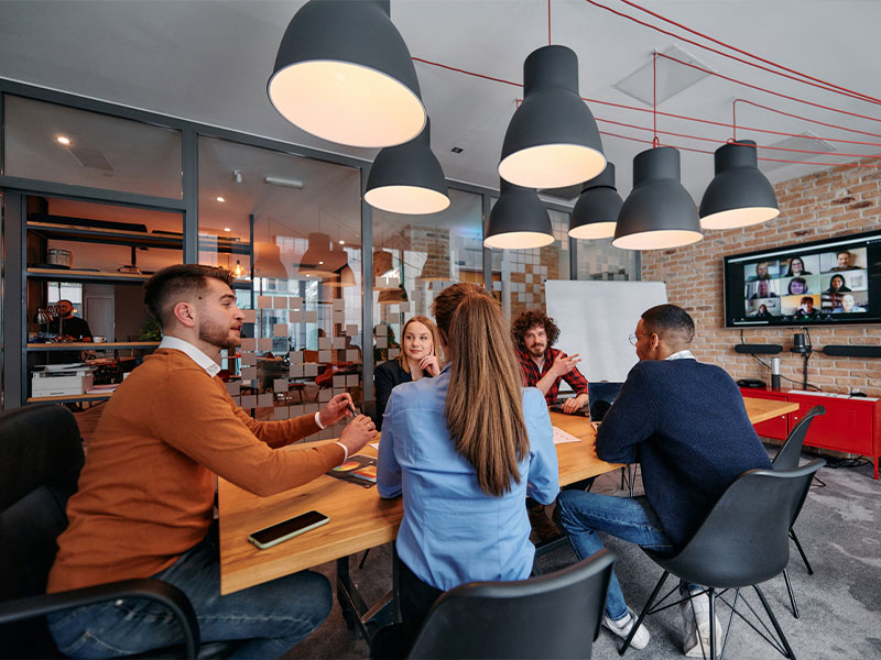 Team meeting in a modern office with virtual call on screen.