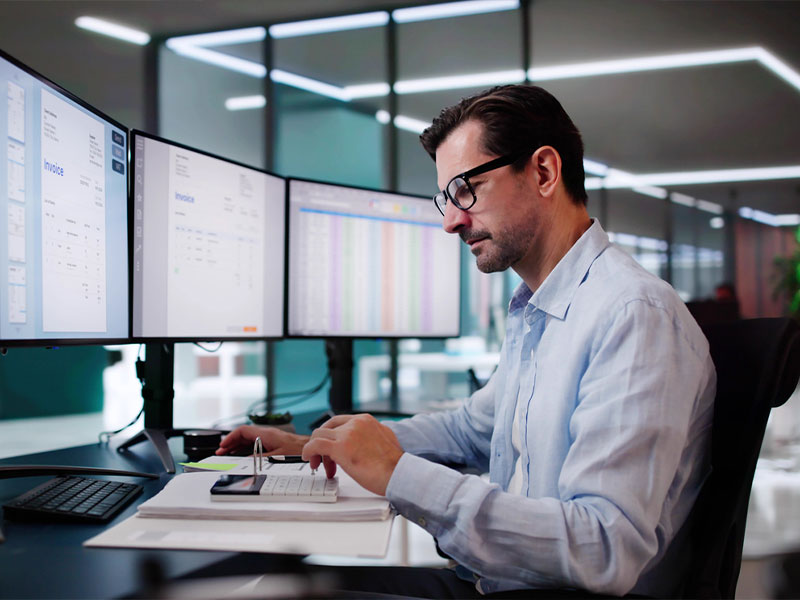 A man working at a desk with multiple computer monitors in an office setting.