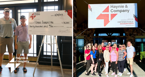 Two men holding a large check alongside a group of people under a Haynie sign at an event.