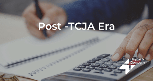 Person calculating finances with notebook and calculator, Post-TCJA Era text.