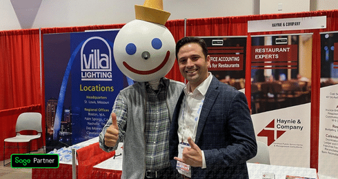 A person with a Jack in the Box mascot head poses with another person at a business expo booth.