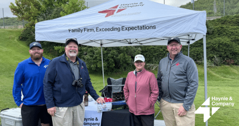 Group of people smiling under a Haynie tent at a golf event.