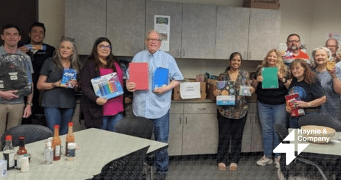 A group of people holding office supplies at Haynie meeting, standing in a room with cabinets and a table.