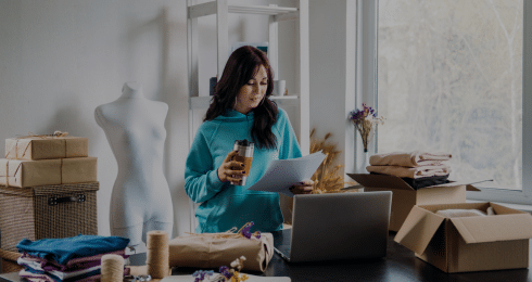 Woman in a blue hoodie working at home office with laptop and papers.
