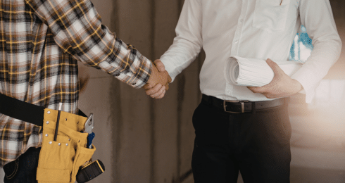 Construction worker and architect shaking hands, holding blueprints, teamwork concept.