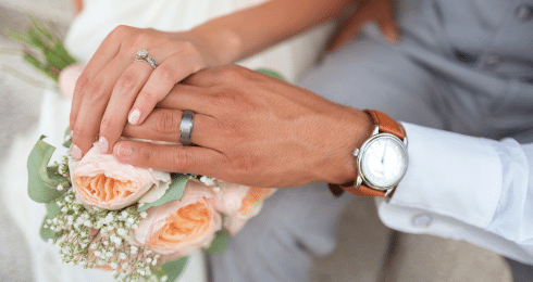 Hands with wedding rings over a bouquet of roses, emphasizing love and commitment.