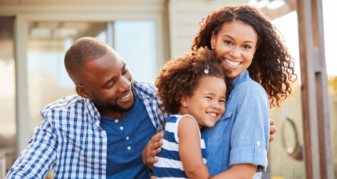 Happy family of three smiling outdoors, embracing and enjoying quality time.
