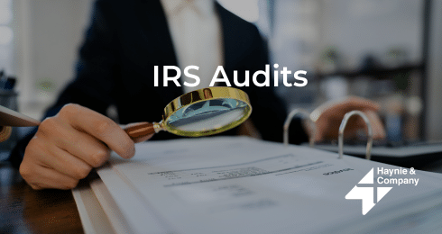 IRS audit documents reviewed with magnifying glass on desk.
