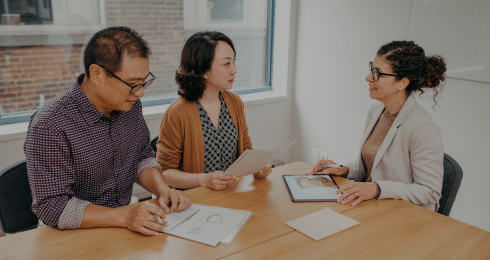 Three people having a business meeting in a conference room with documents and a tablet.