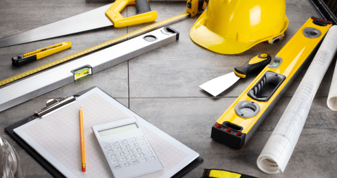 Construction tools, hard hat, and clipboard on a gray surface.