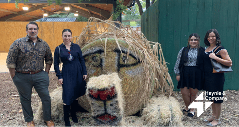 Four people standing beside a large hay sculpture at Haynie outdoor event.