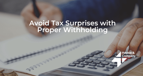 A person calculating taxes with a calculator and pen. Text: Avoid Tax Surprises with Proper Withholding.