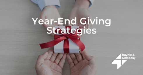 Two people exchanging a gift box with a red ribbon, text Year-End Giving Strategies.
