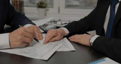 Two people reviewing and signing documents at a desk.