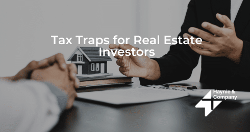 Two people discussing real estate investment tax issues with model house on table.