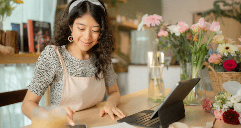 Woman working on tablet in flower shop, surrounded by colorful blossoms.