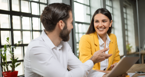 Man and woman in business attire having a discussion in a bright office setting.