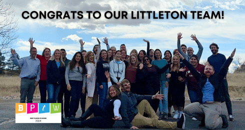 Team celebrating their success in Littleton with arms raised outdoors.