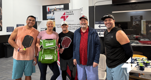 Group of people holding pickleball paddles and gear at an indoor sports facility.