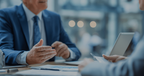 Two people in business suits discuss at a meeting table with documents.
