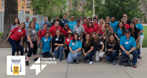 Group of people posing outdoors, wearing Haynie branded shirts, with company logo and awards displayed.