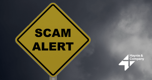 Scam alert sign on a dark cloudy background, Haynie logo.