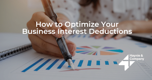 A person writing on financial graphs with How to Optimize Your Business Interest Deductions text.