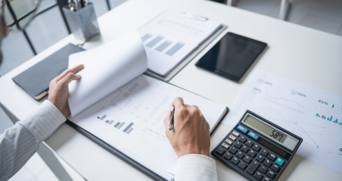 Person reviewing financial reports with a calculator on a desk.