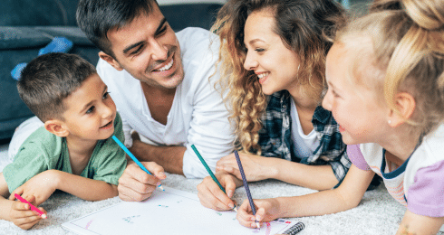Family drawing together on the floor, smiling and enjoying creative time.