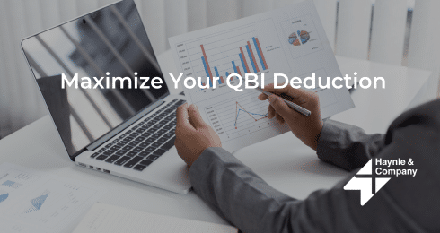 A person reviewing financial graphs beside a laptop with text Maximize Your QBI Deduction.