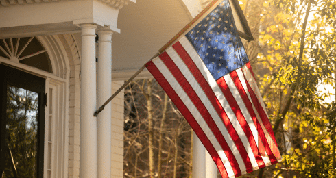 American flag waving on a house porch in the warm sunlight.