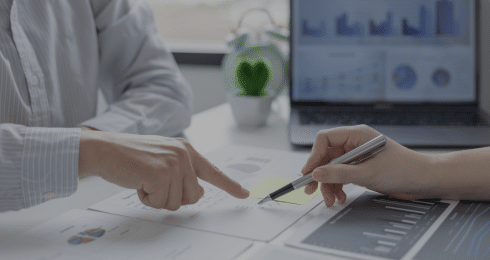 Two people discussing financial graphs at a desk with a laptop in the background.