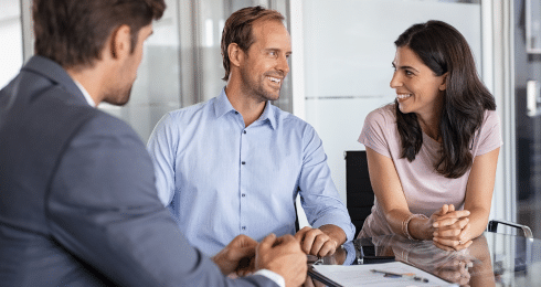 Business meeting with three people discussing at a table in a modern office.