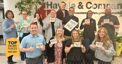 Employees holding awards in an office with Top Workplaces 2020-2022 banner in Haynie background.
