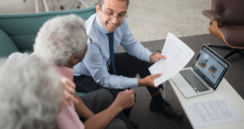 A professional discusses documents with a senior couple next to a laptop.