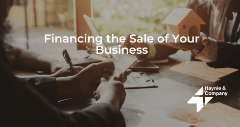 Business sale financing discussion with documents and model house on table.